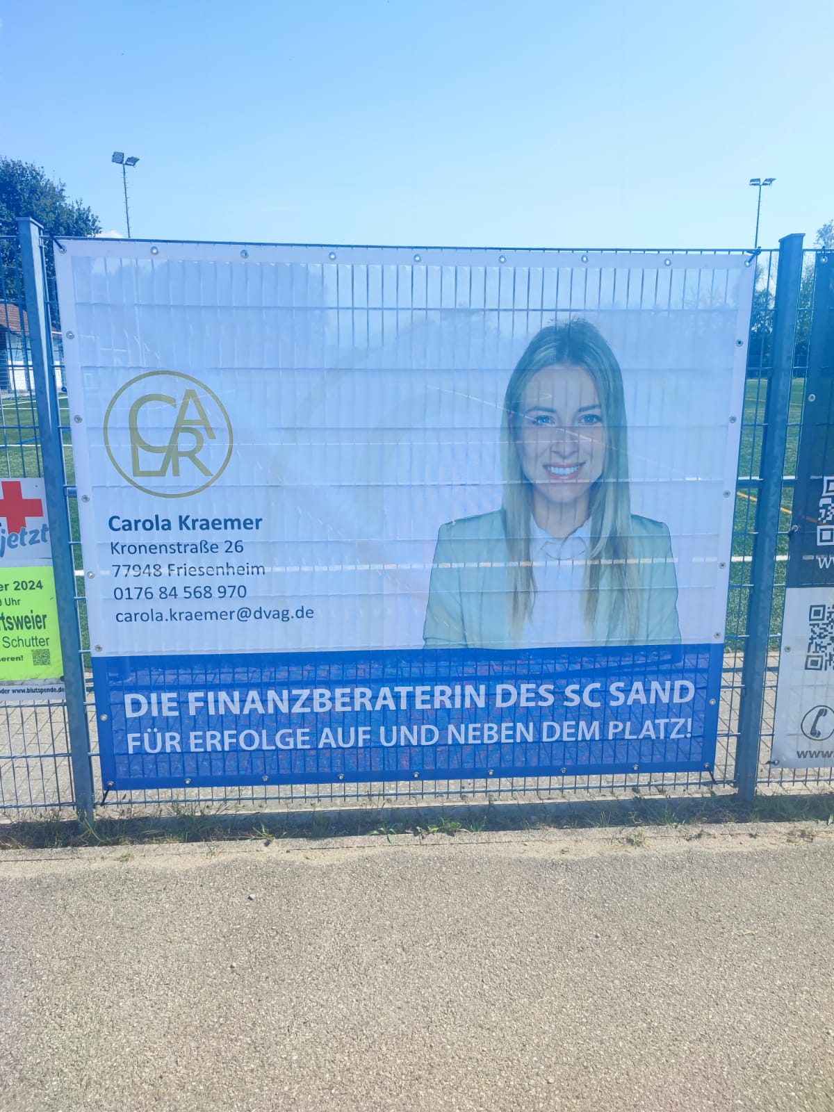 Darstellung eines Banners an einem Zaun mit Kontakdaten, Logo und einer Frau im Anzug